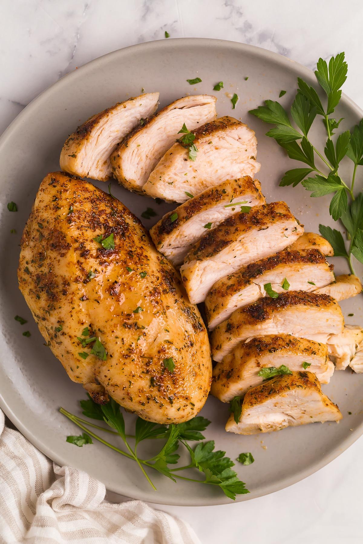 This Air Fryer Chicken Breast is perfectly seasoned and incredibly juicy! It is golden and crispy on the outside and SO flavorful! #chicken #airfryer #recipes #airfryerrecipes plate with one whole chicken breast and one sliced chicken breast.