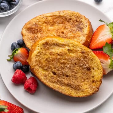 two pieces of french toast on a grey plate with strawberries beside.