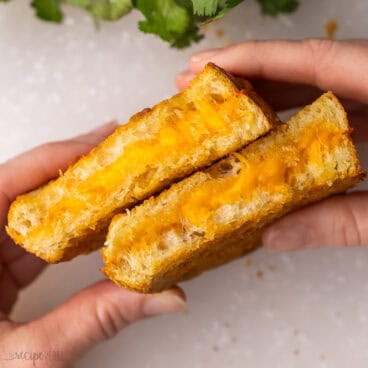 hands holding two halves of a grilled cheese sandwich.