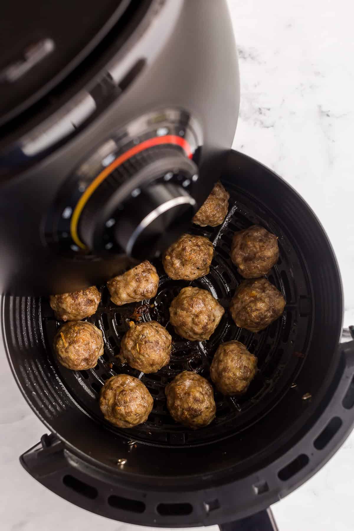 air fryer basket being pulled out with meatballs in the basket.