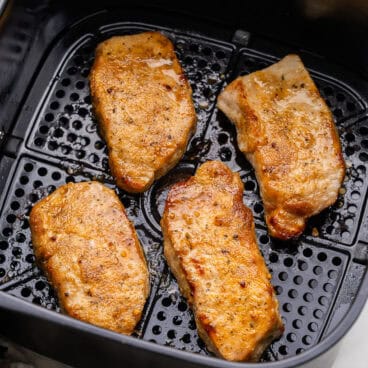 four air fryer pork chops in black air dryer basket.