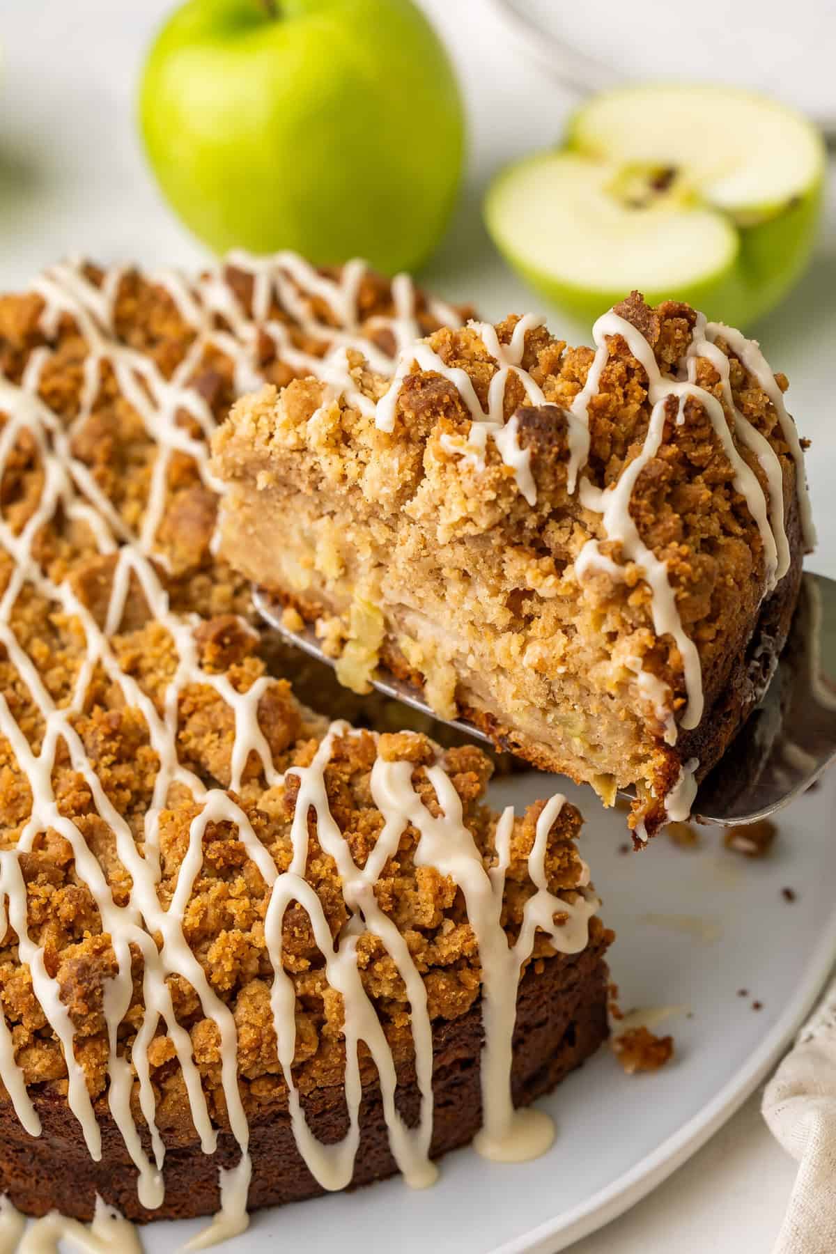 This Apple Coffee Cake with Crumb Topping is the perfect fall breakfast or dessert -- Greek yogurt makes it so moist and it's loaded with apples and the best crunchy brown sugar streusel! #cake #baking #dessert | apple desserts | apple cake | coffee cake recipe | baking from scratch | apple season | apple recipes piece of coffee cake being lifted from the whole.
