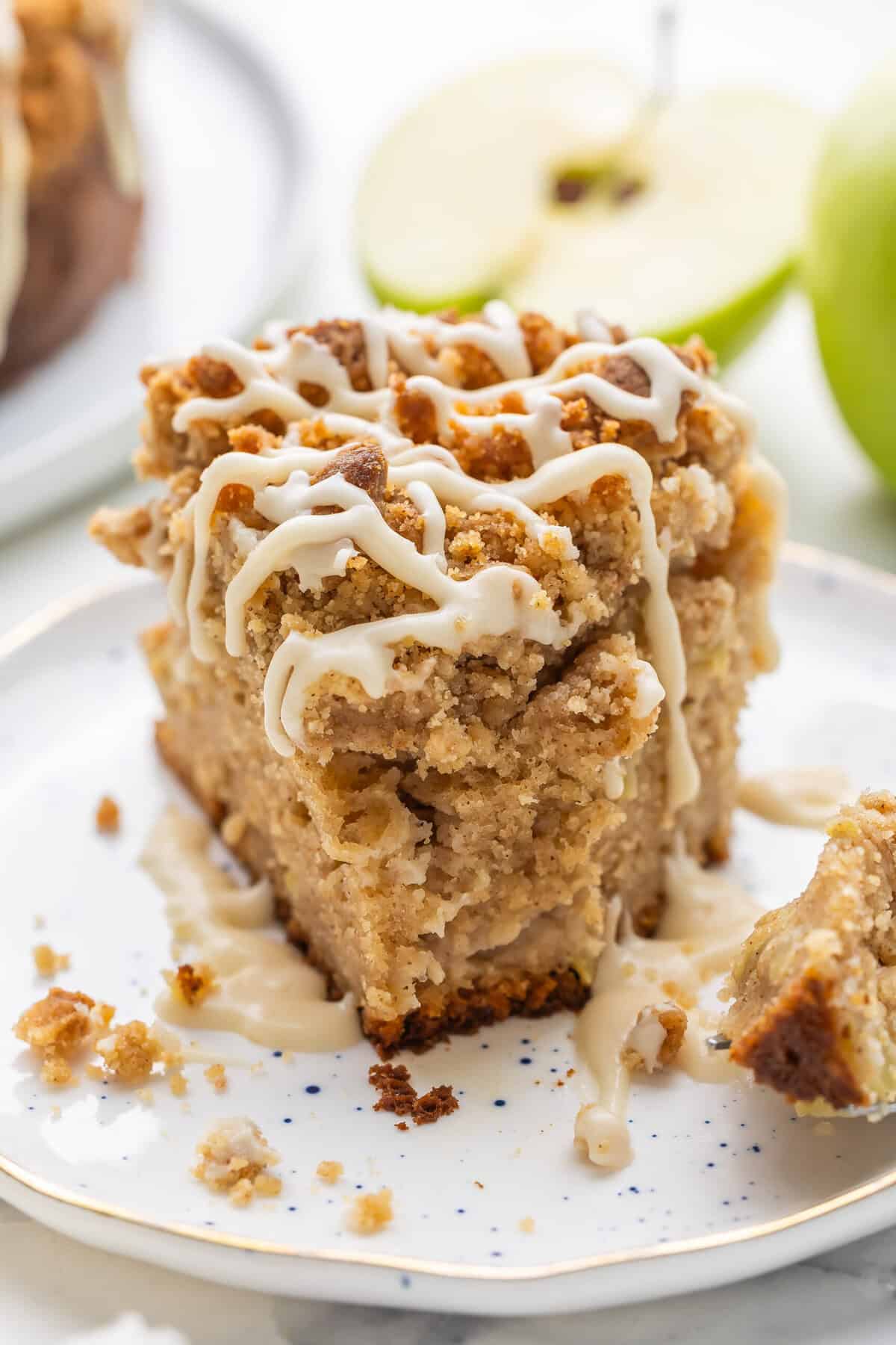 This Apple Coffee Cake with Crumb Topping is the perfect fall breakfast or dessert -- Greek yogurt makes it so moist and it's loaded with apples and the best crunchy brown sugar streusel! #cake #baking #dessert | apple desserts | apple cake | coffee cake recipe | baking from scratch | apple season | apple recipes slice of apple coffee cake with maple glaze with a forkful taken.