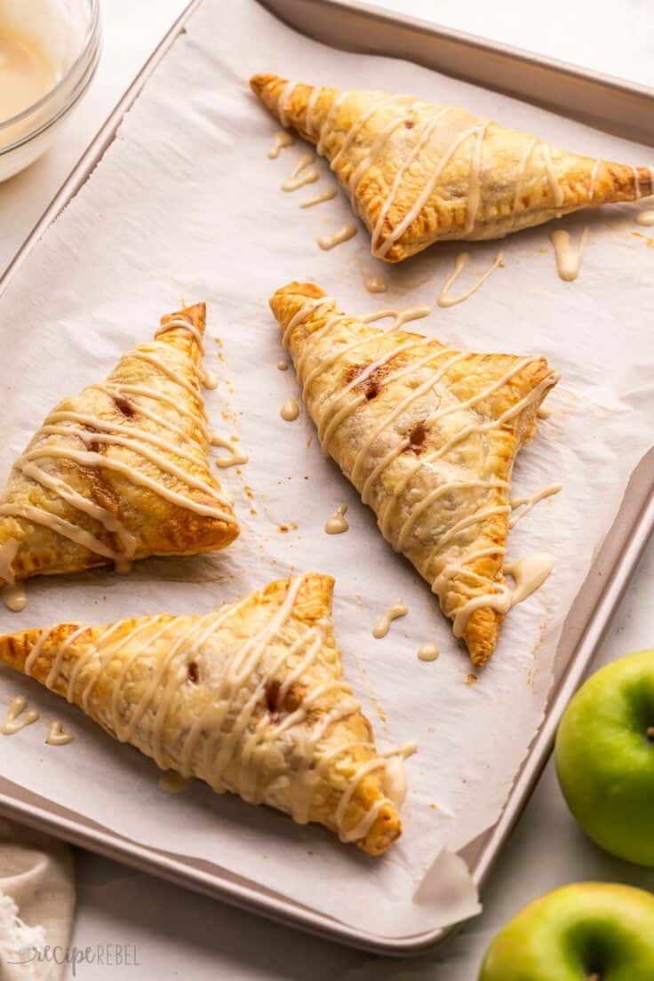 baked apple turnovers on a pan with apples beside.