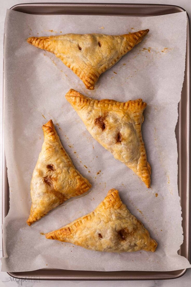 four apple turnovers on a parchment lined pan.