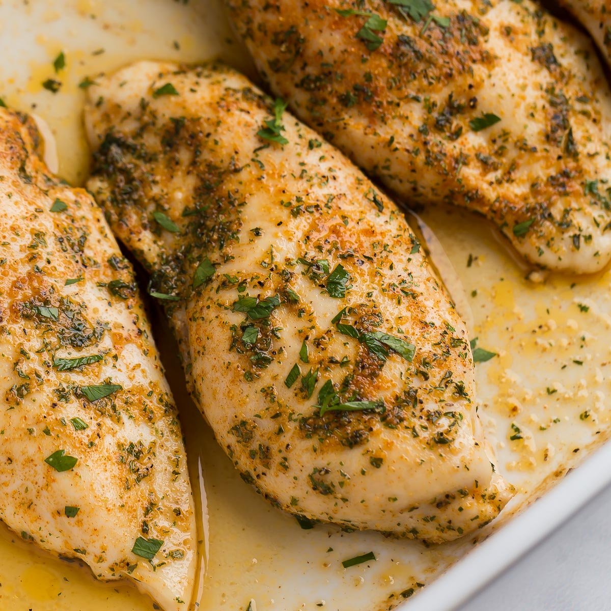 This Baked Chicken Breast comes out juicy and flavorful every time! With a simple spice rub and quick cook time, it's perfect for any night of the week! #chicken #dinner #recipes close up image of baked chicken breasts in baking dish with juices.