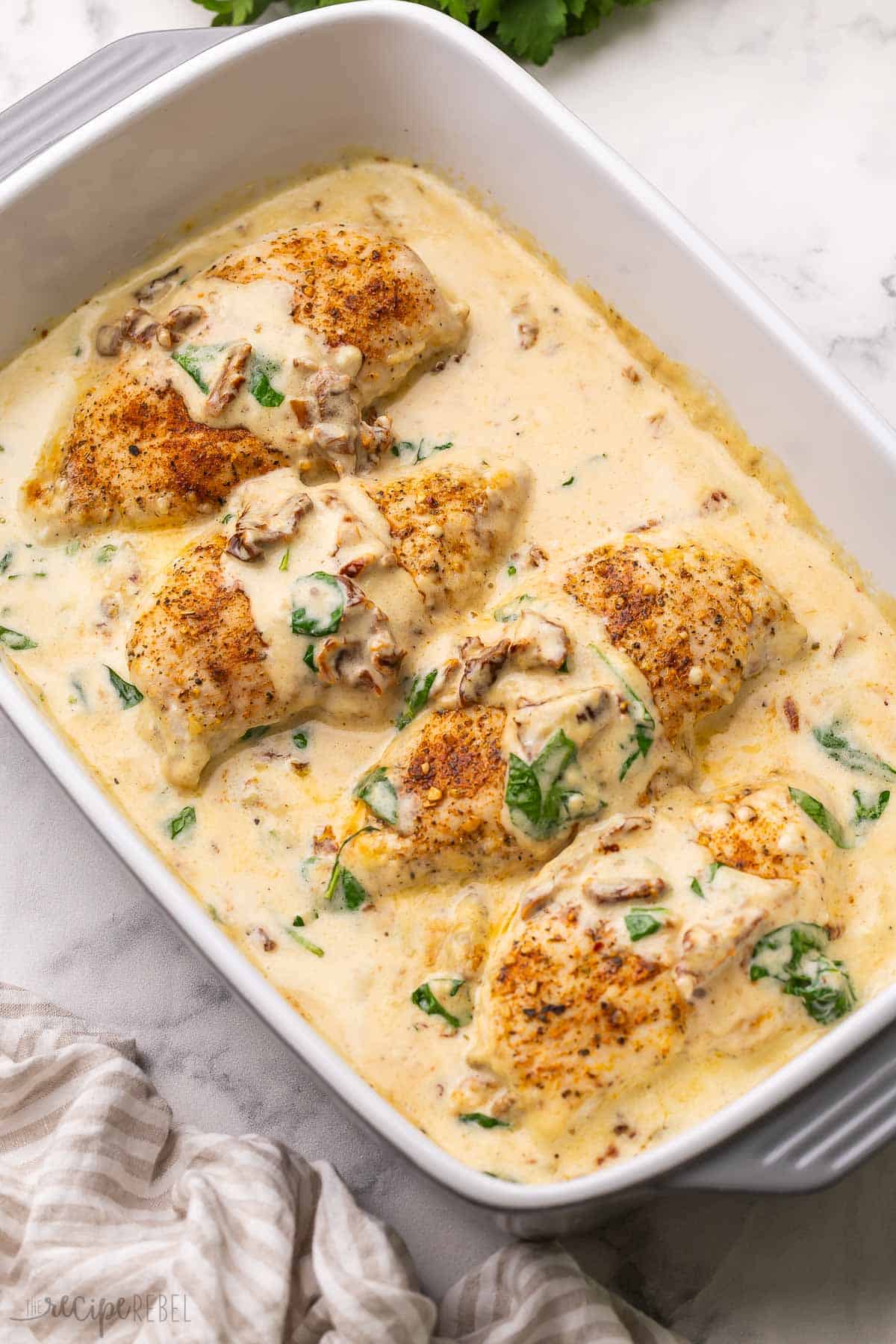 This Baked Tuscan Chicken Breast recipe is an easy meal ready in 30 minutes or less! With a creamy sauce that’s perfect over pasta, it’s one of our favorite chicken breast recipes. #chicken #dinner #recipe | baked chicken breasts | tuscan chicken | creamy chicken | baked chicken breasts | chicken breasts recipe | easy chicken dinner | easy dinner ideas | dinner recipes | how to make chicken breast large dish filled with four baked tuscan chicken breasts.