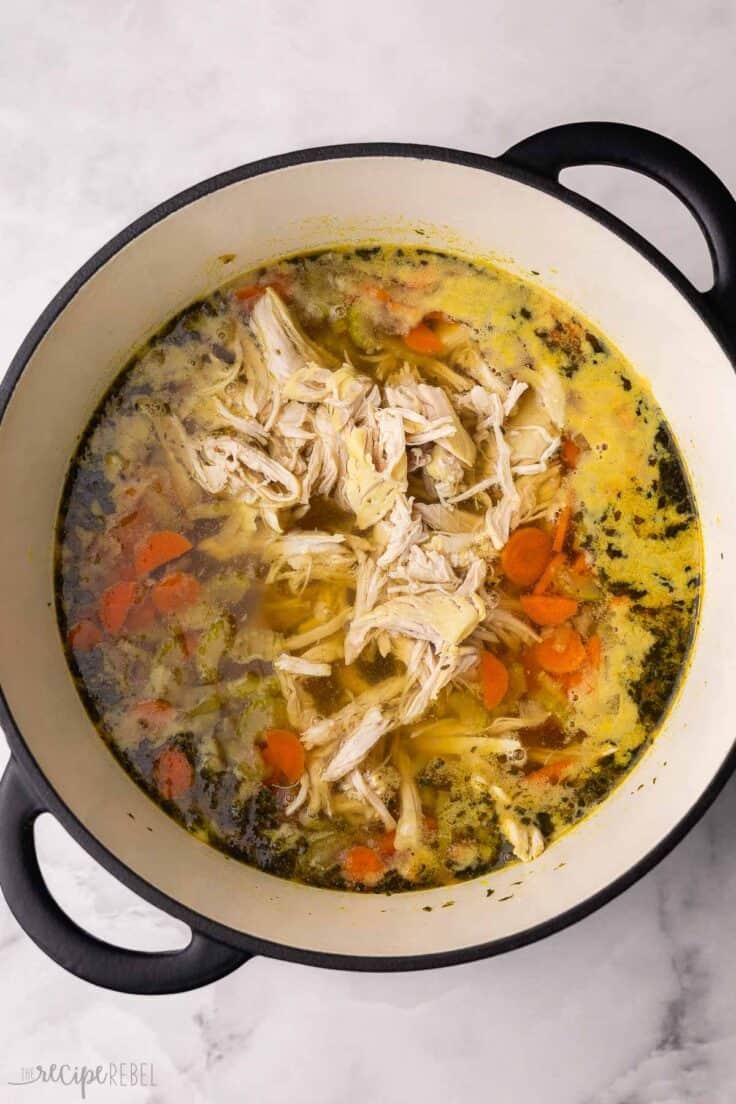 shredded chicken added into pot of chicken noodle soup.