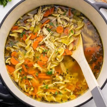 square image of chicken noodle soup in a dutch oven with a wooden spoon.
