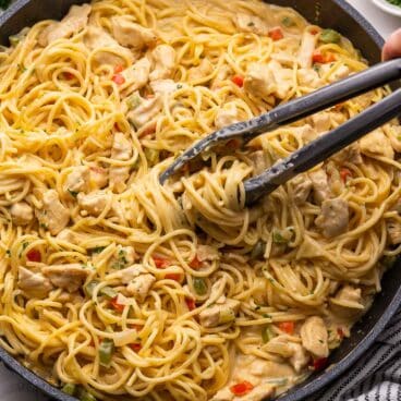 tongs in a large pan of chicken spaghetti.