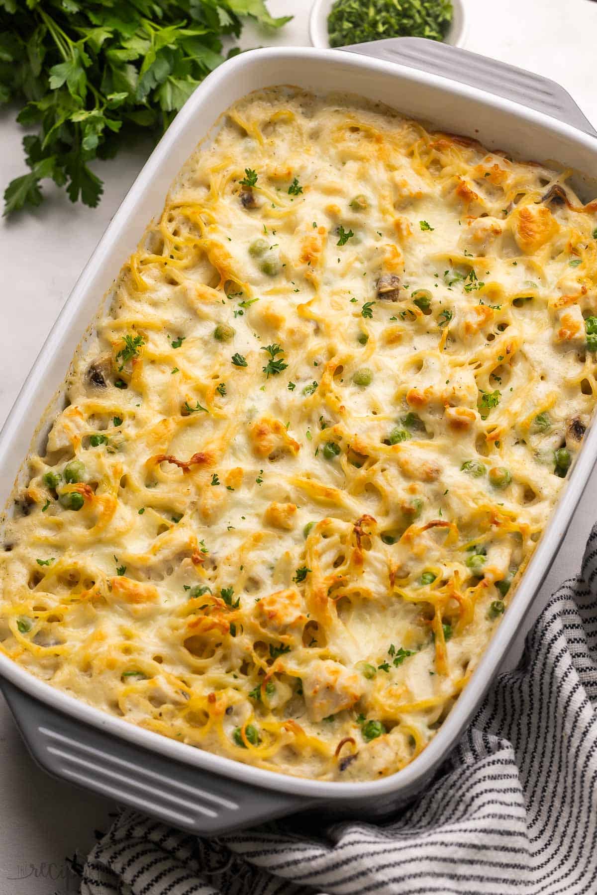 Chicken Tetrazzini is a cozy pasta bake recipe made with tender chicken, sautéed mushrooms, and peas, all tossed in a creamy homemade sauce, topped with mozzarella cheese and baked until golden! It's classic comfort food! #chicken #dinner #pasta | pasta bake | pasta recipe | casserole recipes | comfort food | leftover chicken | chicken pasta | easy dinner ideas | make ahead meal large pan of baked chicken tetrazzini with towel beside.