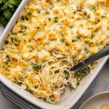 square image of chicken tetrazzini recipe in a white baking dish with scoop.