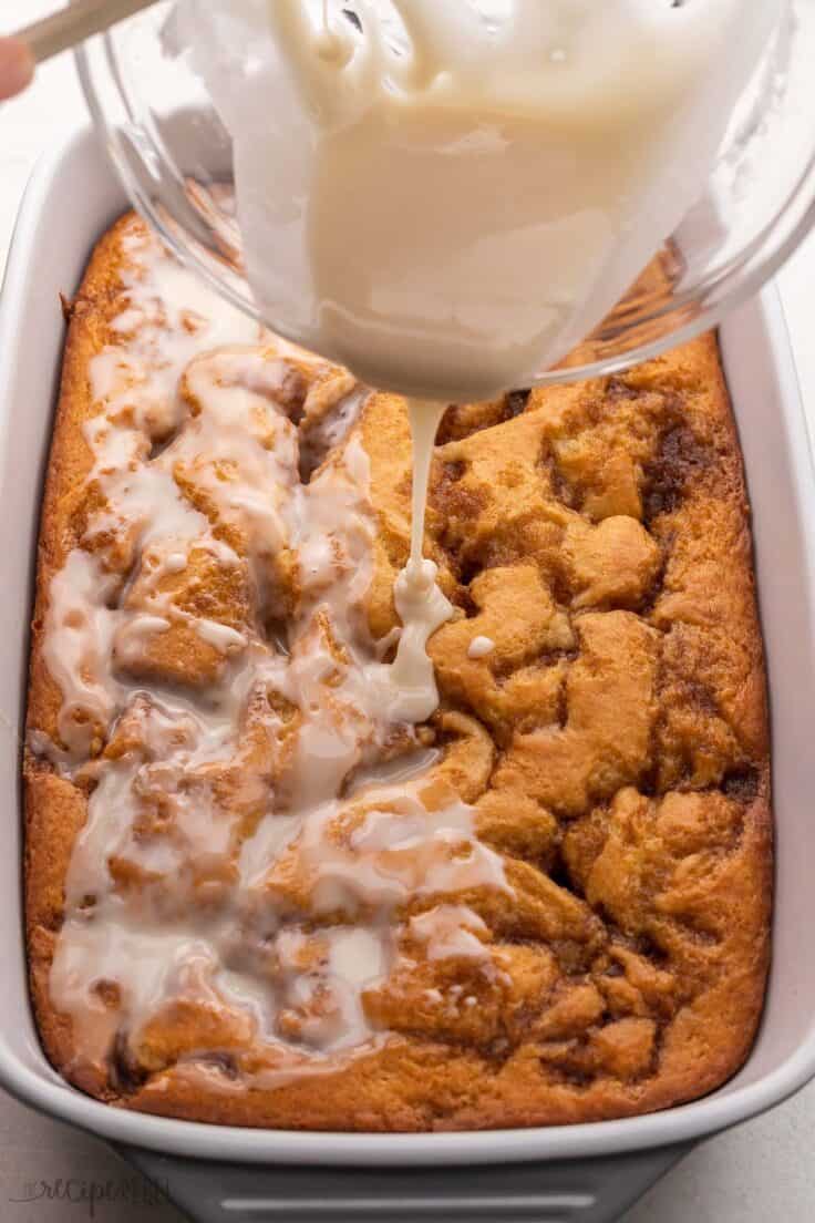 glaze being poured on top of cinnamon roll cake in pan.