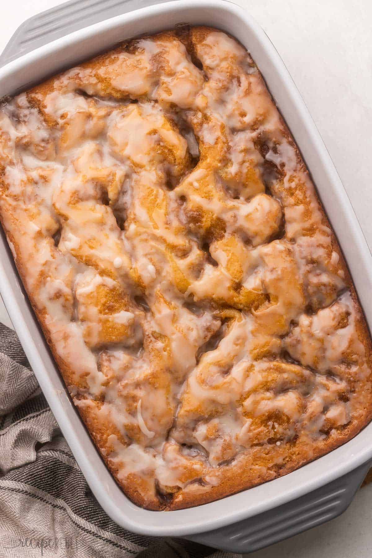 Cinnamon Roll Cake feature a soft homemade cake that's swirled with the most scrumptious cinnamon roll filling! It's baked to perfection in a casserole dish in just 30 minutes before being served with a generous amount of sugary sweet glaze. #cake #dessert #recipe | dessert recipes | cake recipes | cinnamon recipes | brunch | christmas breakfast | christmas dessert | cinnamon roll recipes | thanksgiving breakfast full pan of cinnamon roll cake with glaze on top.