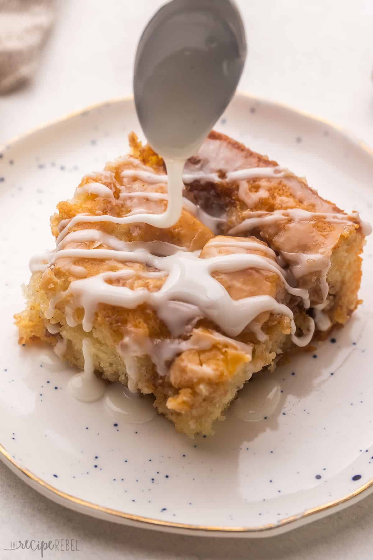 Cinnamon Roll Cake feature a soft homemade cake that's swirled with the most scrumptious cinnamon roll filling! It's baked to perfection in a casserole dish in just 30 minutes before being served with a generous amount of sugary sweet glaze. #cake #dessert #recipe | dessert recipes | cake recipes | cinnamon recipes | brunch | christmas breakfast | christmas dessert | cinnamon roll recipes | thanksgiving breakfast a piece of cinnamon roll cake on a white plate with glaze being drizzled on top.