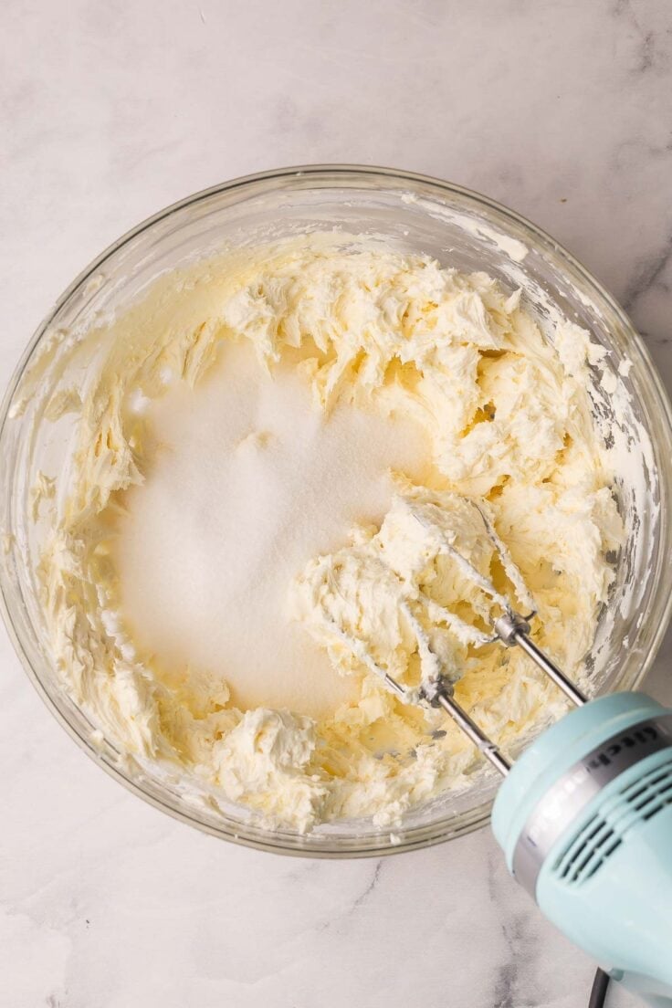 glass mixing bowl with beaten cream cheese and sugar added.
