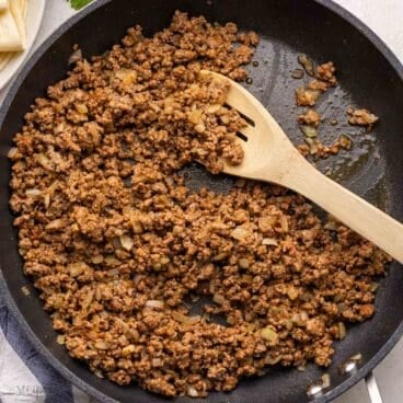 close up of wooden ladle in frying pan full of taco beef.