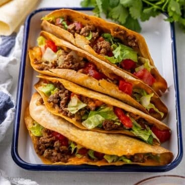 four crispy baked tacos in a white dish.