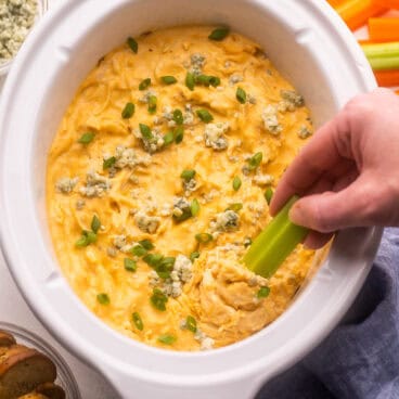 close up of a celery stick scooping buffalo chicken dip out of crockpot.
