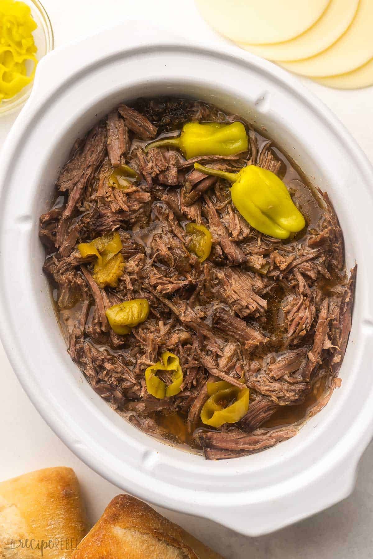 Easy shredded Italian Beef made in the crockpot, just six ingredients! Tender chuck roast is simmered in a tangy broth for fall-apart goodness, perfect for serving on sandwiches. Includes Instant Pot method and step-by-step video. #slowcooker #crockpot #recipe #dinner | beef roast recipe | beef recipe | roast beef | mississippi beef | sandwich recipe | crockpot dinner shredded italian beef in crockpot with peppers on top.