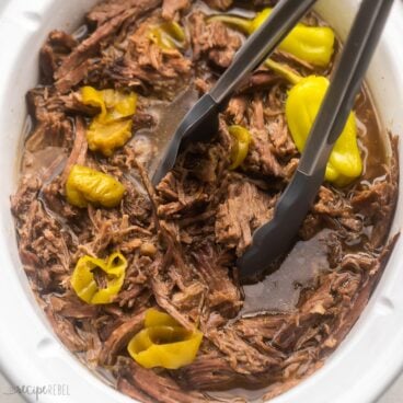 italian beef being lifted out of white crockpot with tongs.