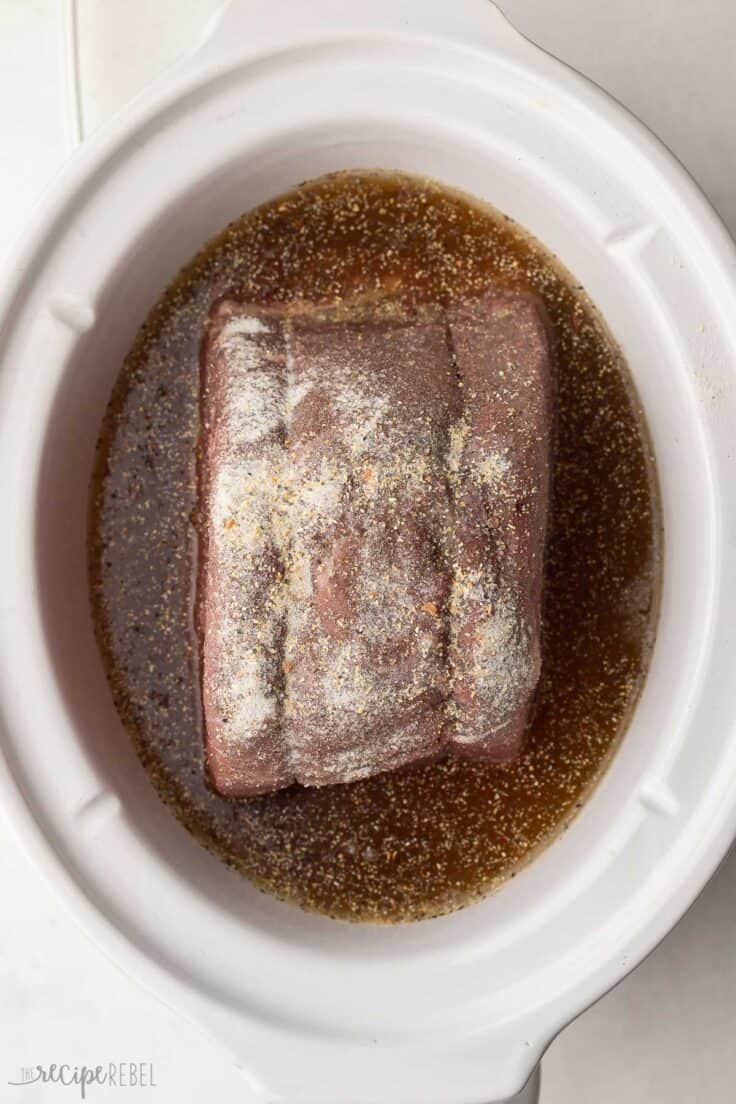 beef roast and liquid in white crockpot.