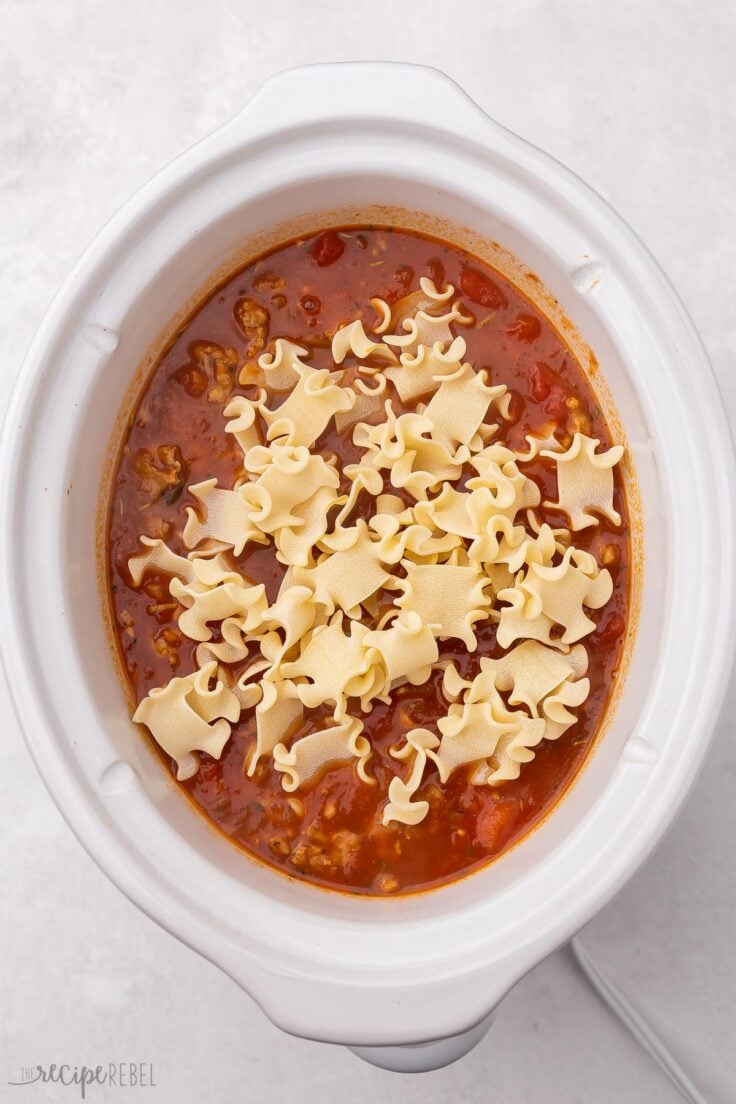 white crockpot with lasagna soup in it and broken lasagna noodles on top.