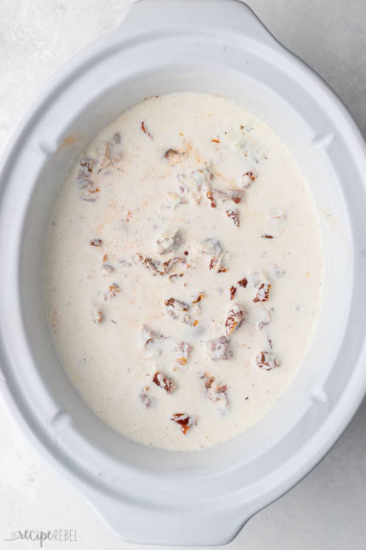white slow cooker filled with chicken breasts and sauce.
