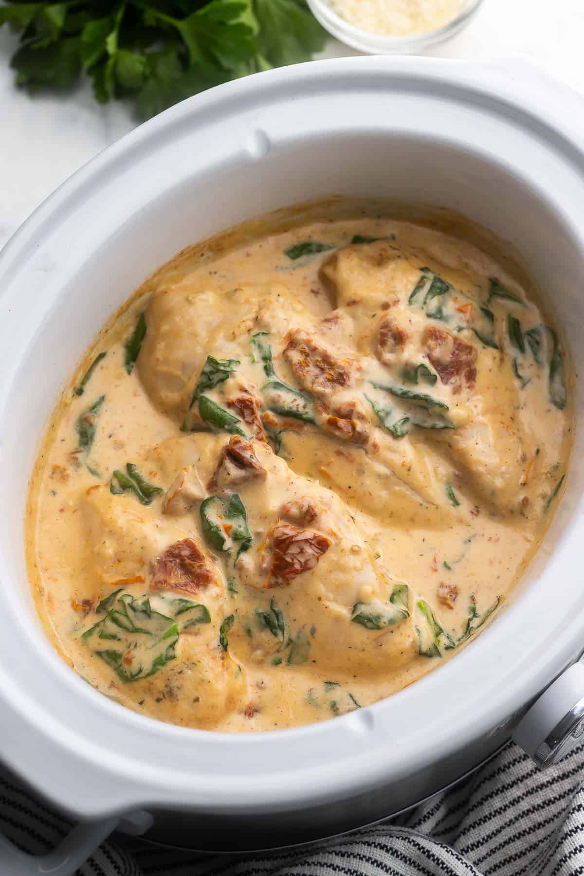 This Crockpot Tuscan Chicken features juicy chicken breasts slow cooked in a rich and flavorful cream sauce. This recipe takes just 10 minutes to prep and makes the perfect dinner served over your favorite pasta! #crockpot #slowcooker #recipe #dinner | dinner ideas | chicken recipes | chicken dinner | crockpot chicken | slow cooker chicken recipes | easy chicken breast recipes close up image of chicken breasts in the crockpot with tuscan sauce.