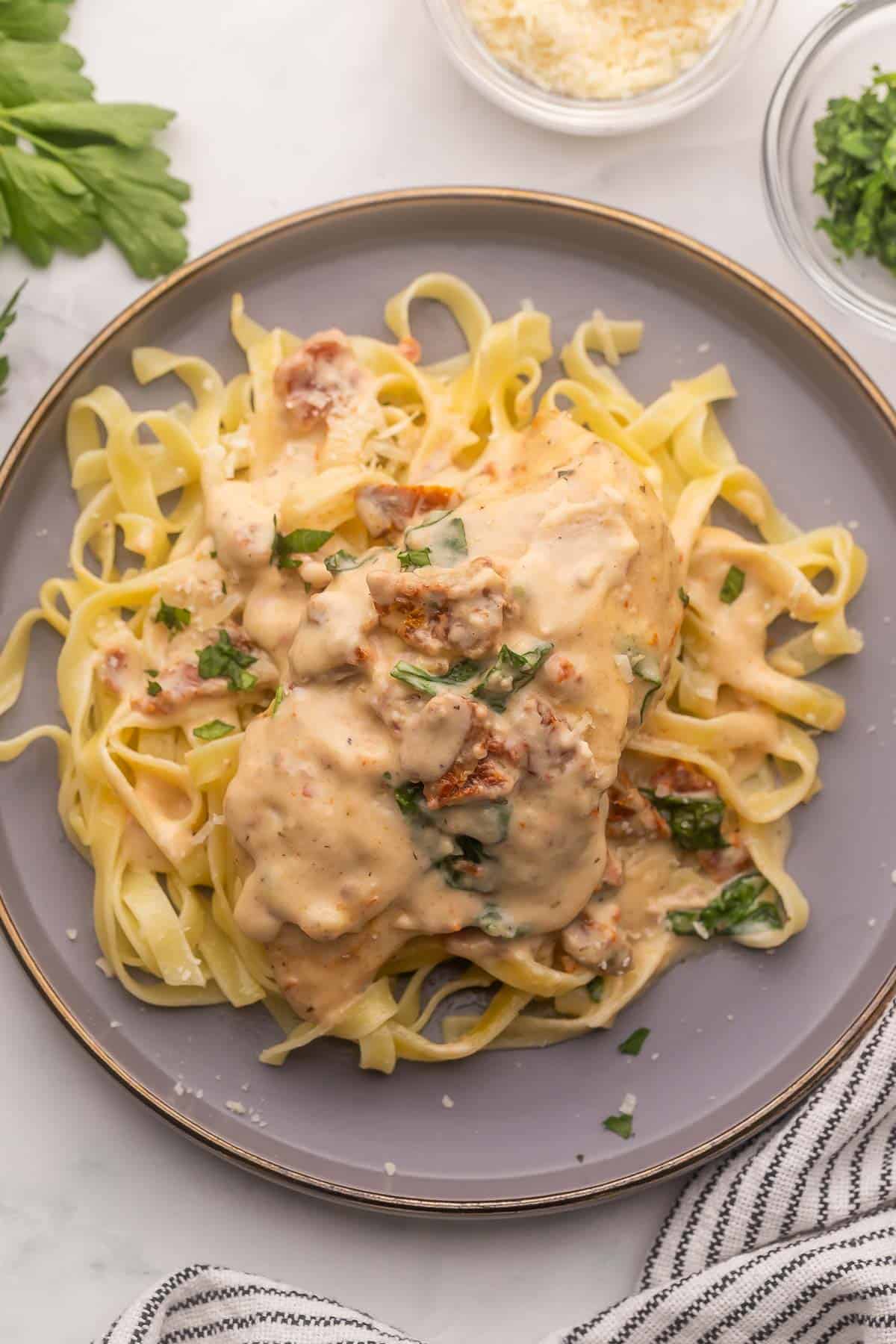 This Crockpot Tuscan Chicken features juicy chicken breasts slow cooked in a rich and flavorful cream sauce. This recipe takes just 10 minutes to prep and makes the perfect dinner served over your favorite pasta! #crockpot #slowcooker #recipe #dinner | dinner ideas | chicken recipes | chicken dinner | crockpot chicken | slow cooker chicken recipes | easy chicken breast recipes overhead image of tuscan chicken breast over fettuccine.