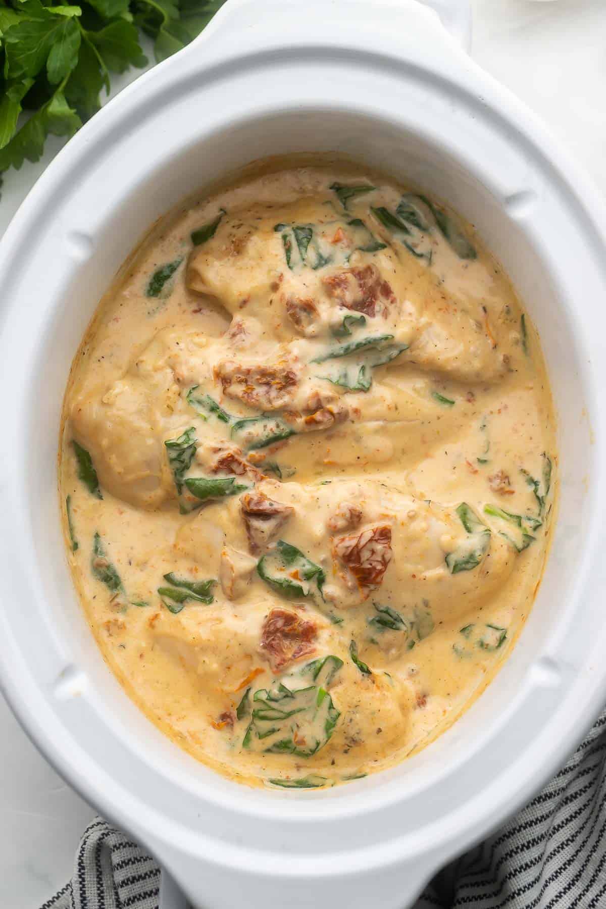 This Crockpot Tuscan Chicken features juicy chicken breasts slow cooked in a rich and flavorful cream sauce. This recipe takes just 10 minutes to prep and makes the perfect dinner served over your favorite pasta! #crockpot #slowcooker #recipe #dinner | dinner ideas | chicken recipes | chicken dinner | crockpot chicken | slow cooker chicken recipes | easy chicken breast recipes overhead image of crockpot tuscan chicken in white slow cooker.