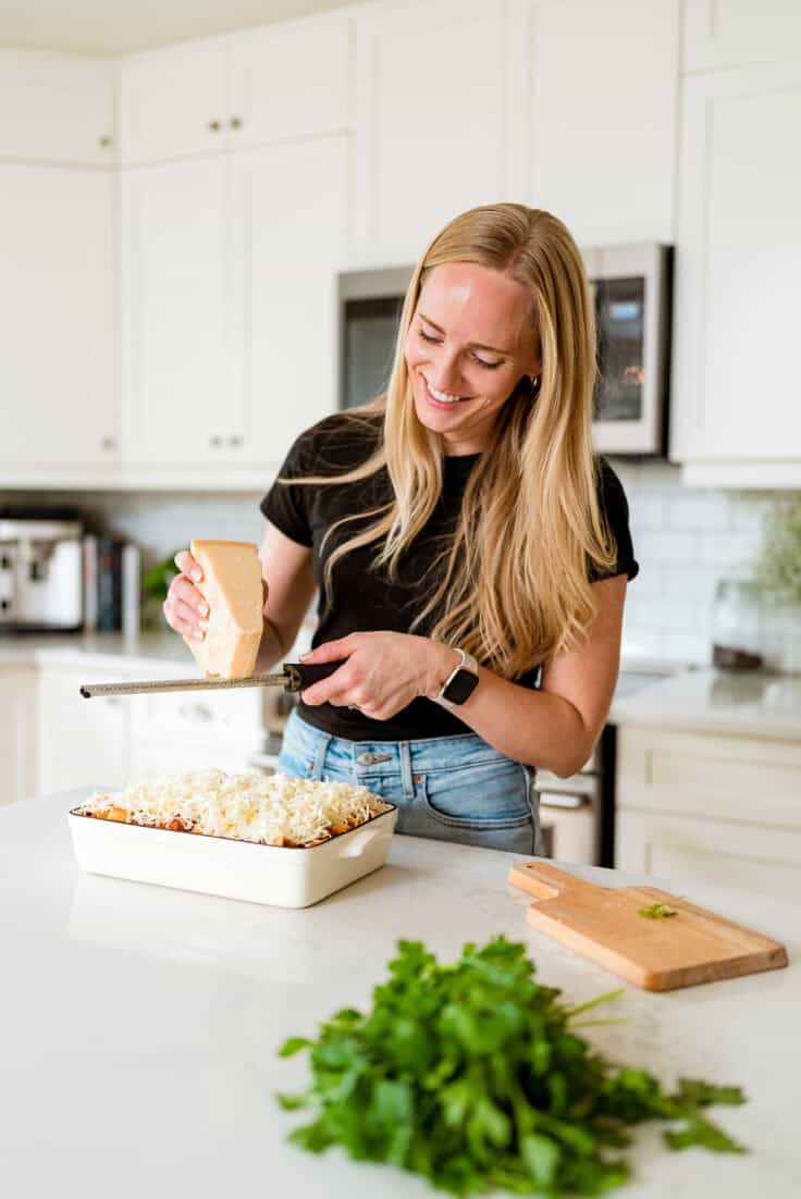 Ashley standing in a white kitchen grating cheese.