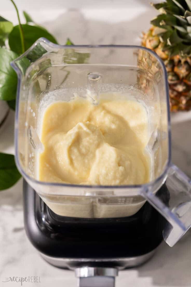 a full blender of pina colada slushy with a pineapple behind.