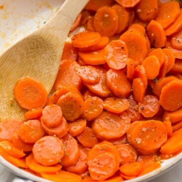 square image of glazed carrots in a white skillet with a wooden spoon.