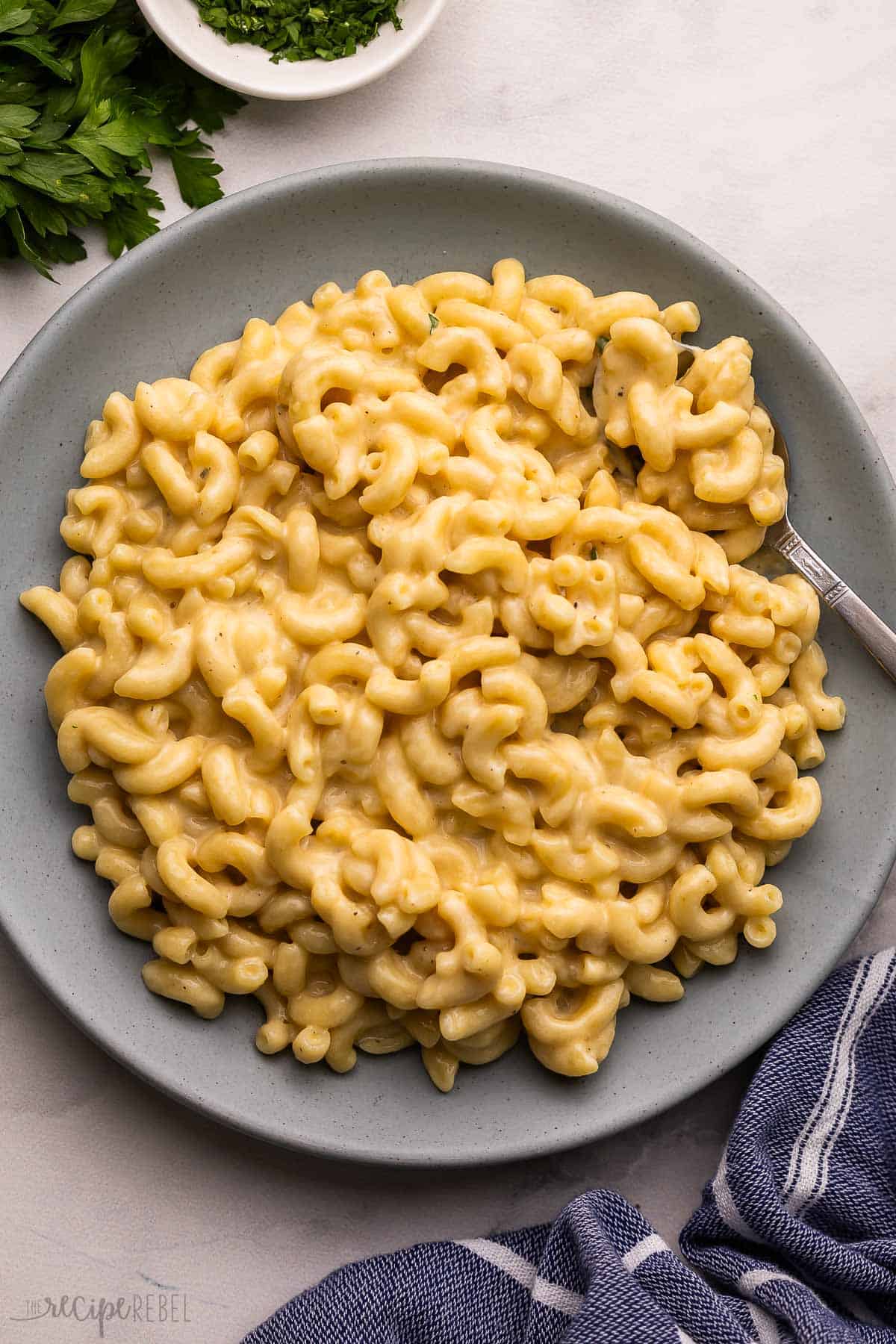 This Easy Homemade Mac and Cheese is super cheesy and creamy, made with a few ingredients all in one pot! Ready in 30 minutes or less, this stovetop mac is a family favorite. #dinner #recipe | macaroni and cheese | skillet mac and cheese | easy macaroni and cheese | comfort food | easy dinner recipes | one pot pasta blue plate filled with mac and cheese and a fork.