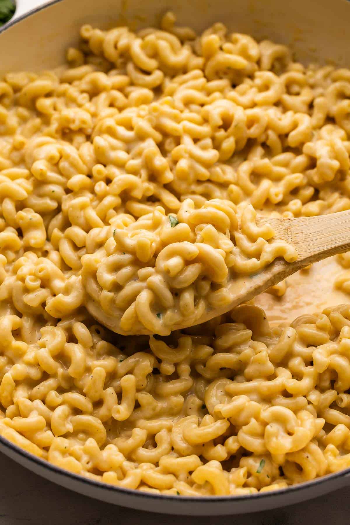 This Easy Homemade Mac and Cheese is super cheesy and creamy, made with a few ingredients all in one pot! Ready in 30 minutes or less, this stovetop mac is a family favorite. #dinner #recipe | macaroni and cheese | skillet mac and cheese | easy macaroni and cheese | comfort food | easy dinner recipes | one pot pasta wooden spoon scooping skillet macaroni and cheese from pan.