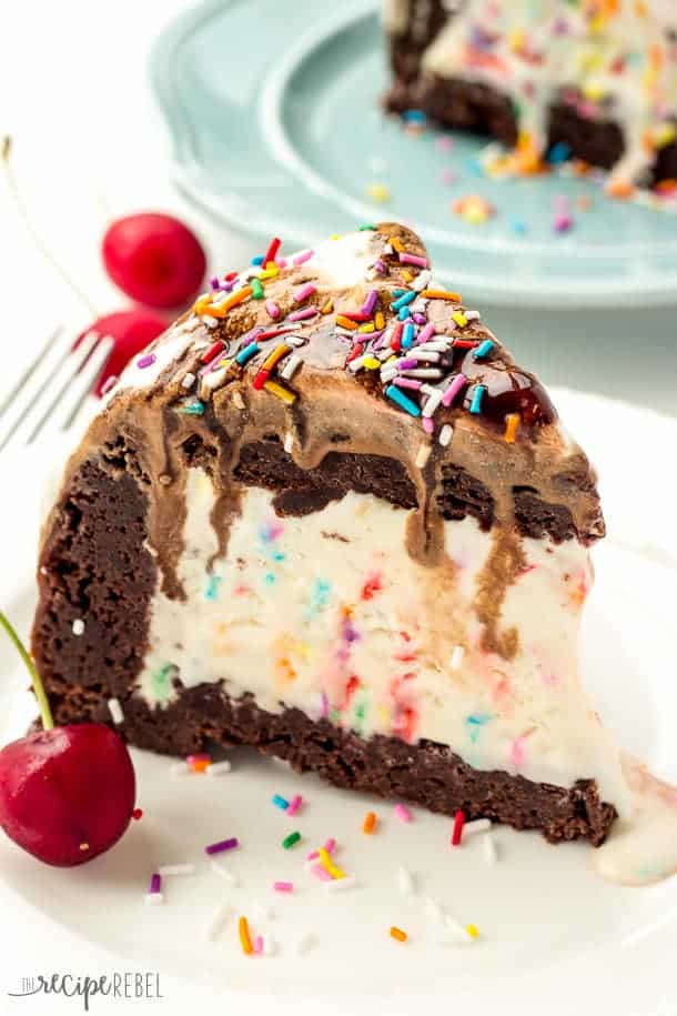 Ice Cream Brownie Mountain: A fun new ice cream cake! Rich, fudgy brownies filled with homemade ice cream (or use store bough and keep it simple!) and topped with chocolate ganache, whipped cream, chocolate sauce and sprinkles -- the perfect cake for a birthday or celebration! Change up the ice cream flavors to suit your tastes! www.thereciperebel.com slice of brownie mountain ice cream cake with sprinkle ice cream in the middle and brownies all around
