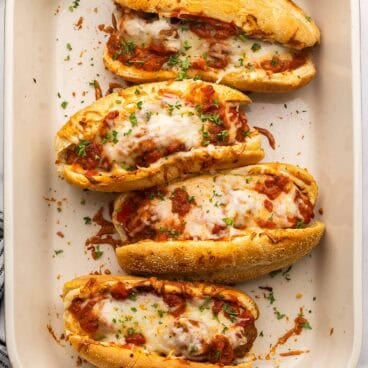 square overhead image of four meatball subs in a baking dish.