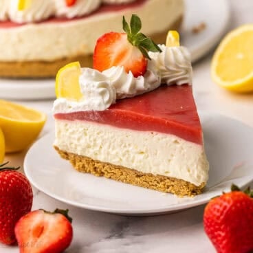 a piece of strawberry lemonade cheesecake on a white plate with the cake in the background.