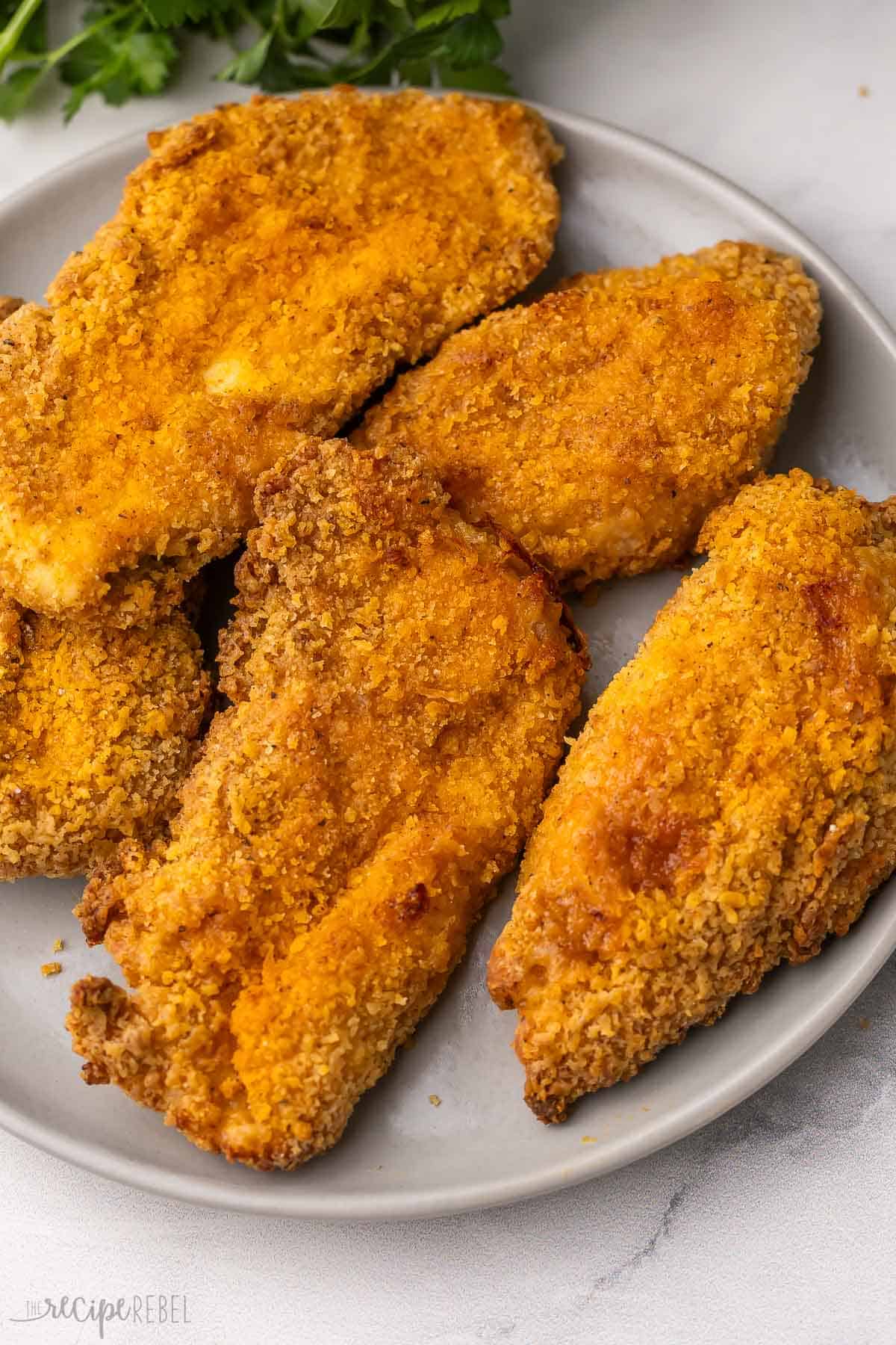 This easy Oven-Fried Chicken turns out perfectly crispy and juicy every time! The special seasoning blend tastes just like KFC, but it’s made with wholesome ingredients in your own kitchen. No deep fryer needed! #chicken #dinner #recipe | baked fried chicken | fried chicken breast | KFC copycat | chicken breast recipes | easy dinner ideas a plate filled with oven fried chicken with parsley behind.