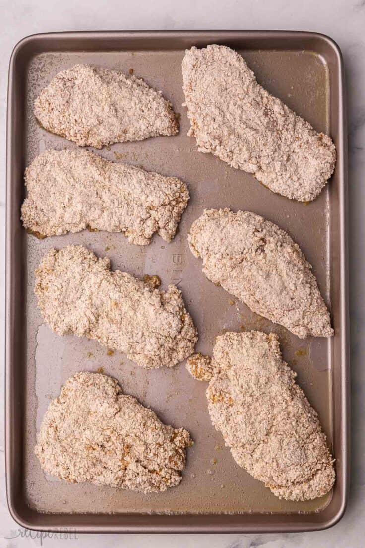 coated pieces of uncooked chicken on large baking sheet.
