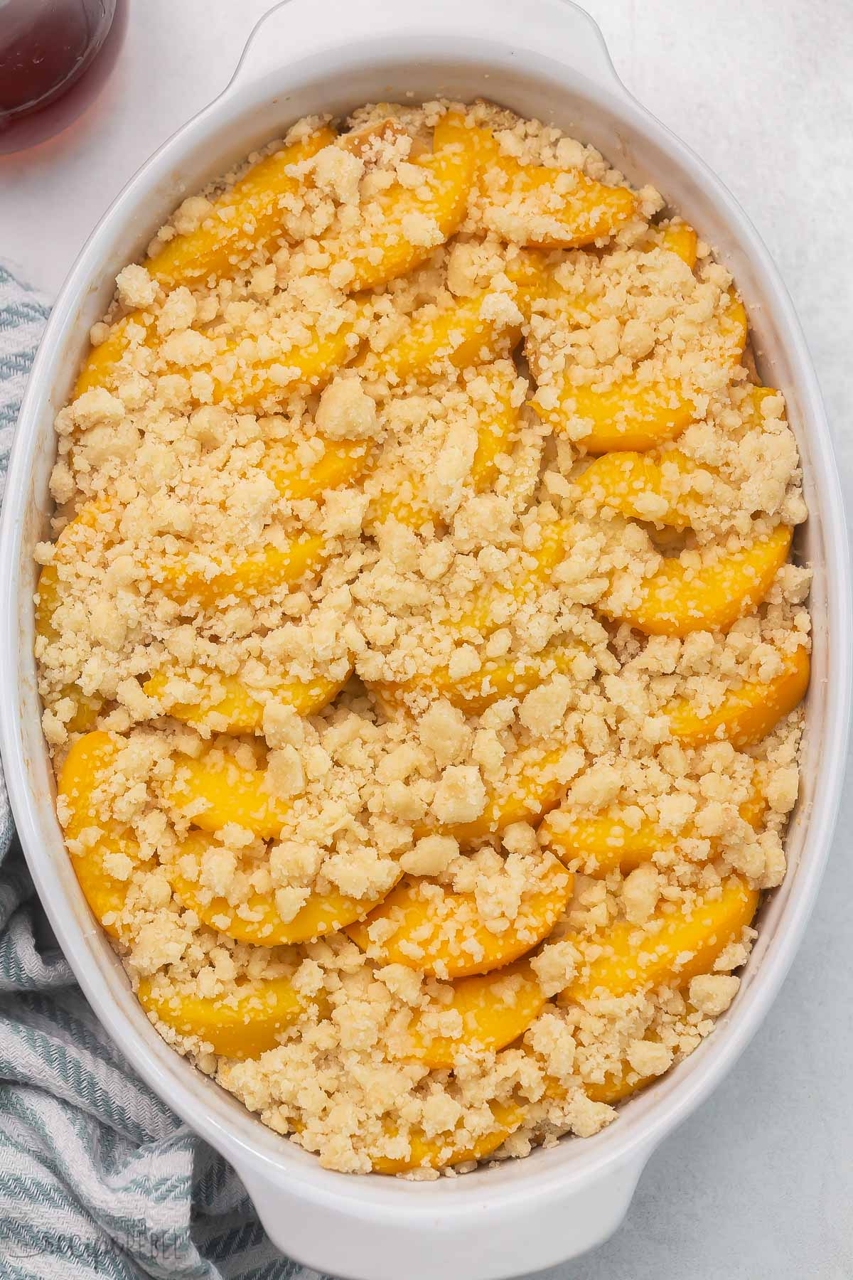 An easy Overnight French Toast Casserole topped with peach cobbler — it's the BEST French toast I’ve ever had! So perfect for Spring, it's full of juicy peaches and a sweet, moist crumb topping! #peaches #recipe | breakfast recipe | brunch ideas | easter brunch | canned peaches | fresh peaches | french toast casserole Top view of Peach Cobbler French Toast in a casserole dish.