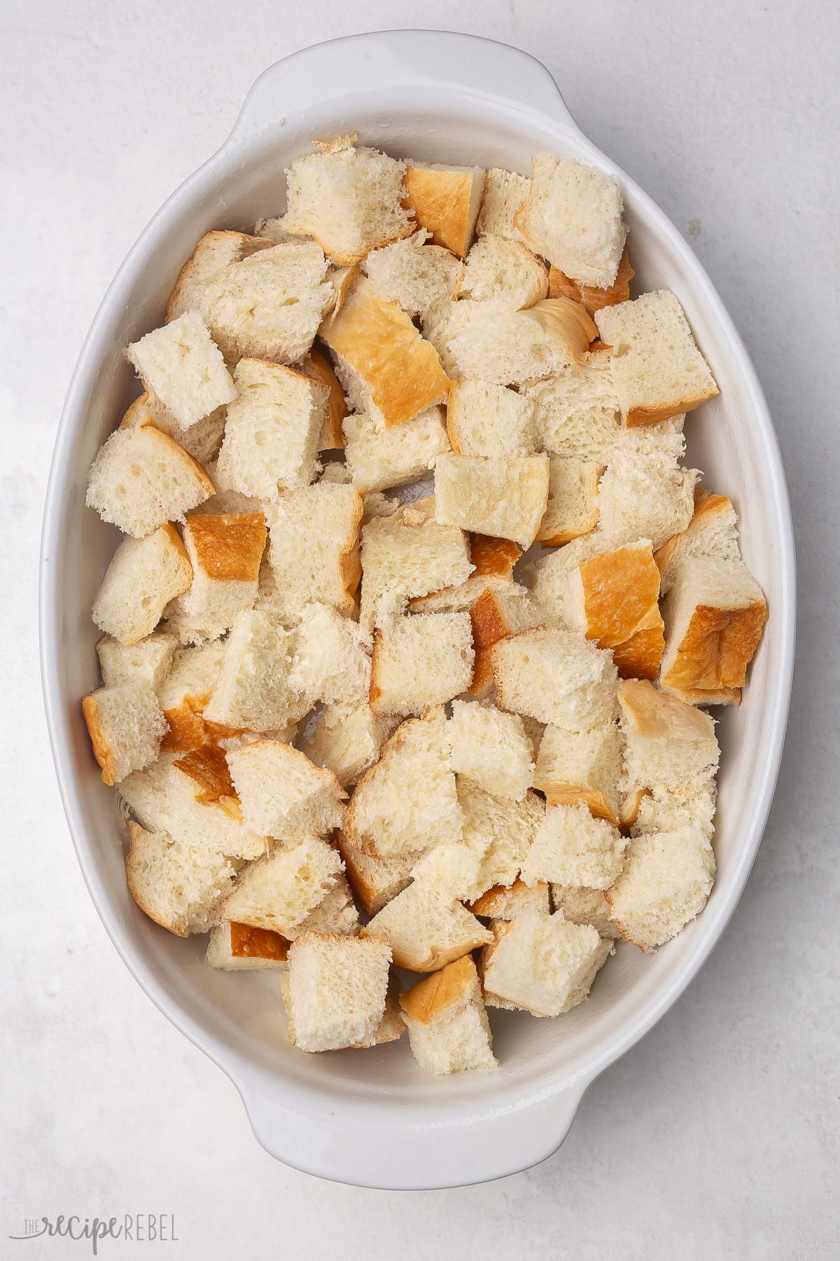 Top view of a casserole dish with cubes of bread lining the bottom in a single layer.