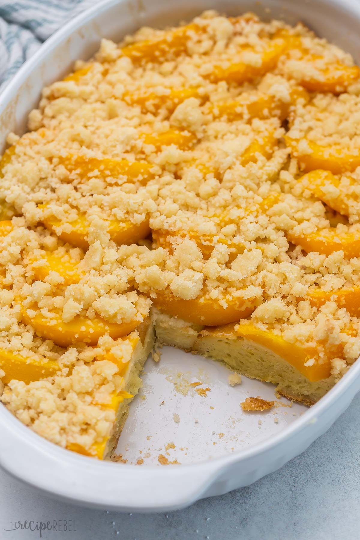 An easy Overnight French Toast Casserole topped with peach cobbler — it's the BEST French toast I’ve ever had! So perfect for Spring, it's full of juicy peaches and a sweet, moist crumb topping! #peaches #recipe | breakfast recipe | brunch ideas | easter brunch | canned peaches | fresh peaches | french toast casserole Top view of peach cobbler French toast in a casserole dish with a slice taken out of it