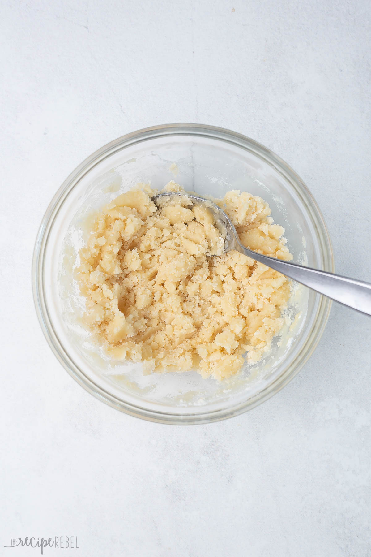 Top view of a small mixing bowl with cobbler topping and a silver spoon in it.