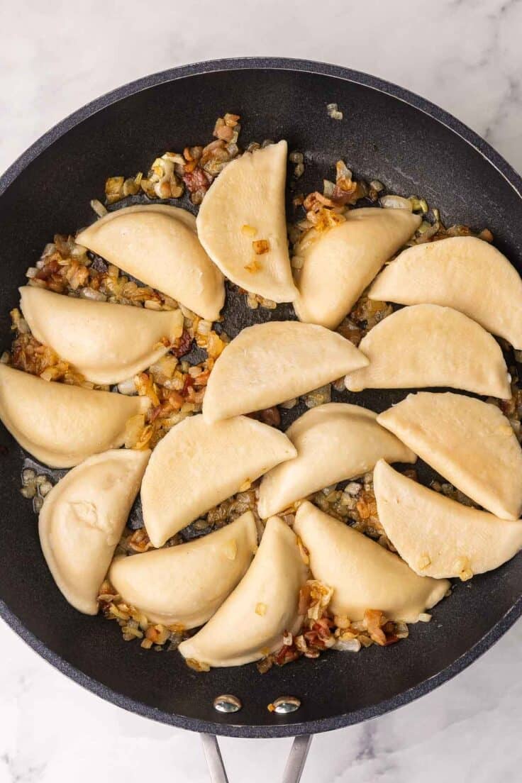 cooked perogies added to black pan with onions and bacon.