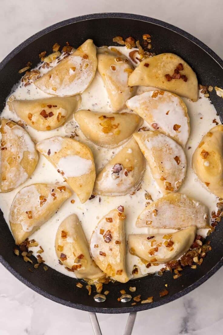 cream added to perogies and other ingredients in pan.