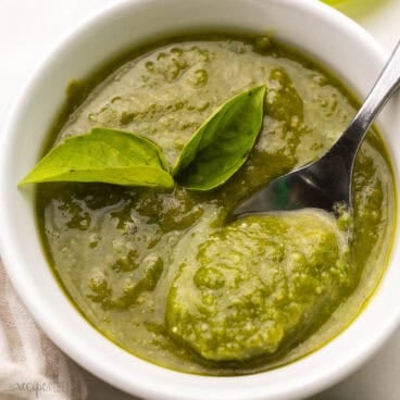 basil leaves on homemade basil pesto in a white bowl.