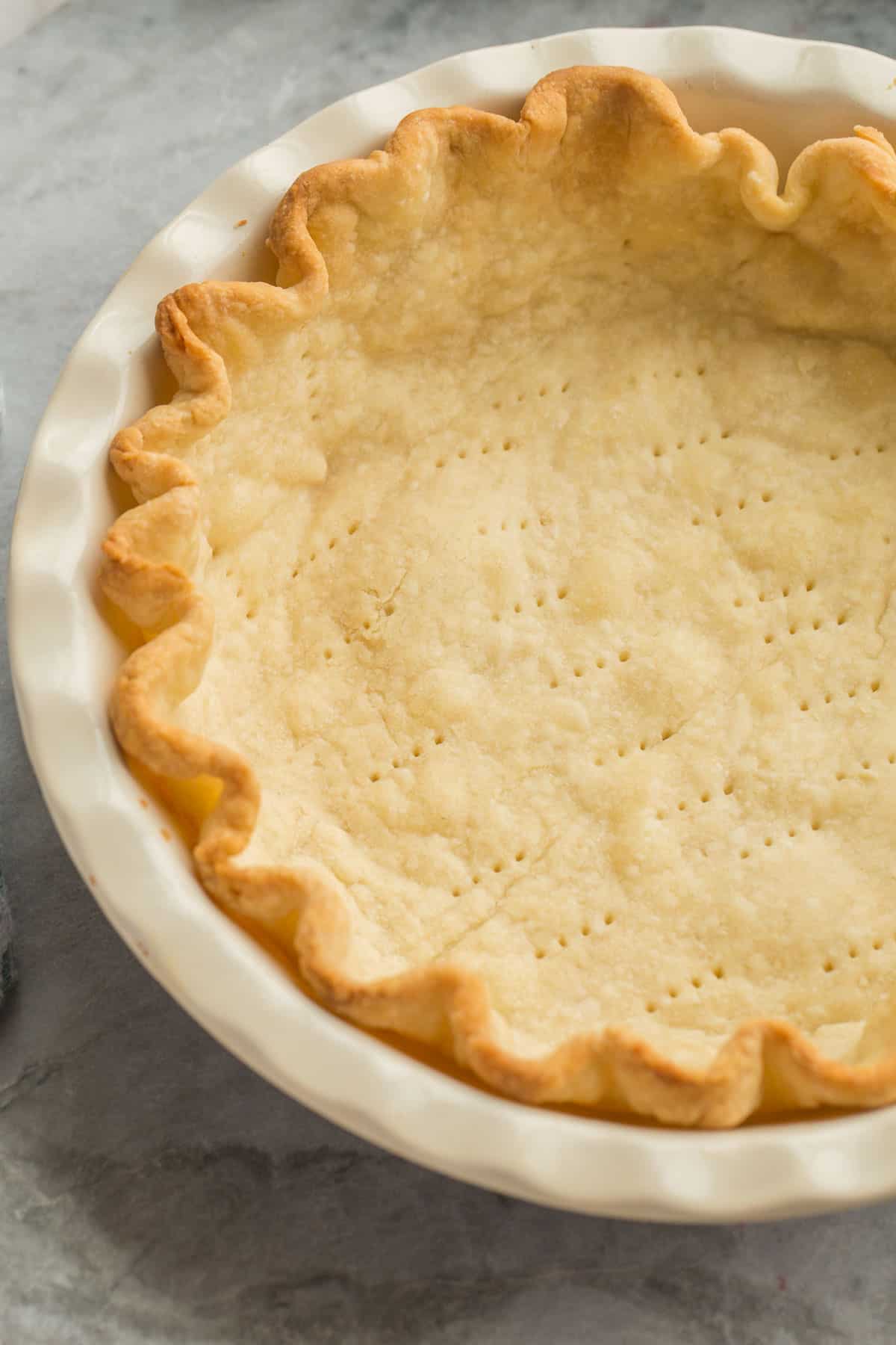 This easy Pie Crust recipe is golden and buttery -- perfect for any pie! Make it by hand or in the food processor, plus tips for storage and freezing. #dessert #recipe | baking recipe | pie recipes | pie crust recipe | how to make pie crust | pie pastry | easy pastry | thanksgiving dessert | christmas baking close up image of blind baked pie crust in pie plate.
