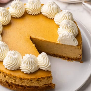 pumpkin cheesecake topped with whipped cream on a white plate.